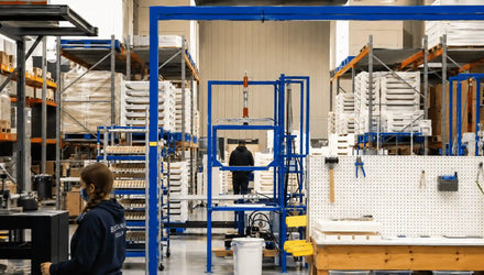 Soap manufacturing facility with workers, curing racks, production equipment, and organized storage systems for large-scale soap production.